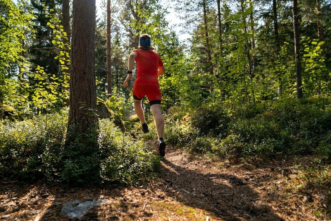 Hardloper in rood tenue loopt over een bospad tijdens een rustige duurloop