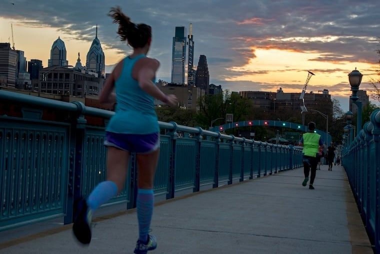 Lopers rennen over een brug bij zonsondergang, met stadsgebouwen op de achtergrond
