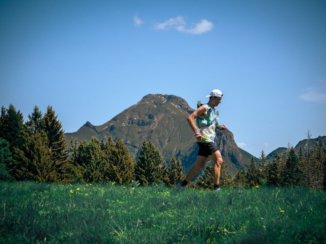 Trailrunner rent door een alpenweide met berg en bos op de achtergrond